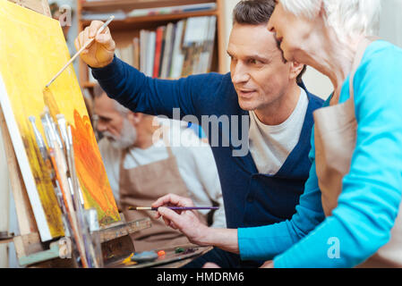 Delighted artist showing elderly woman how to paint. Stock Photo