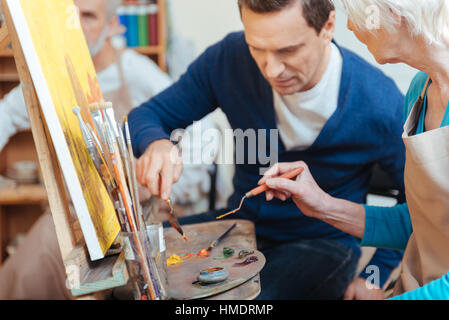 Delighted artist helping elderly woman in painting Stock Photo