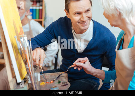 Friendly artist helping elderly woman in painting Stock Photo