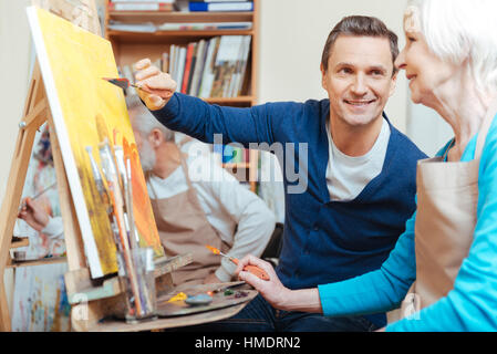 Overjoyed artist helping elderly woman in painting Stock Photo