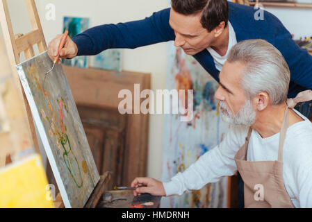 Concentrated artist helping elderly man in painting Stock Photo