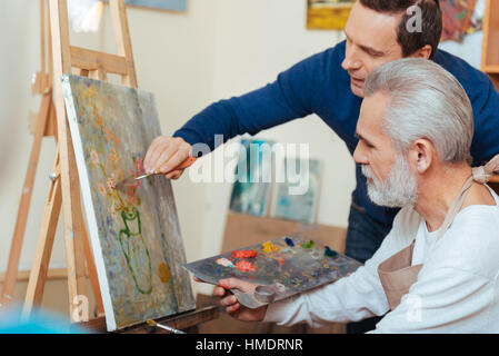 Young artist helping elderly man in painting Stock Photo