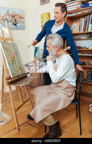 Ambitious artist helping elderly man in painting Stock Photo