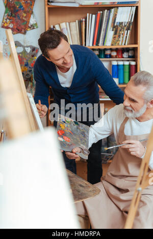 Smiling artist helping elderly man in painting Stock Photo