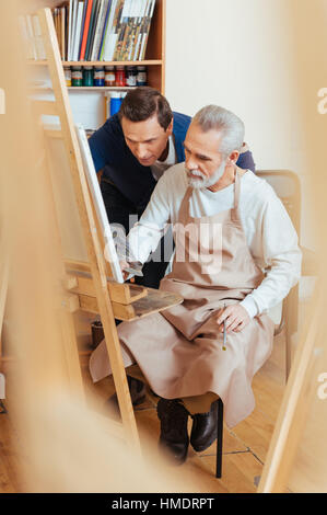 Talented artist helping elderly man in painting Stock Photo