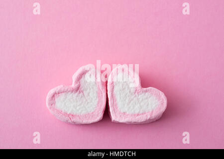 two pink and white heart-shaped marshmallows on a pink background Stock Photo