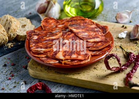 closeup of an earthenware plate with some slices of spanish chorizo, cured pork sausage, some slices of bread, a glass cruet with olive oil and some g Stock Photo