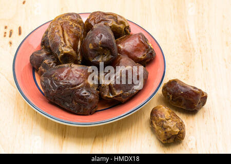Pile of dried dates fruit in red plate on a wooden board Stock Photo