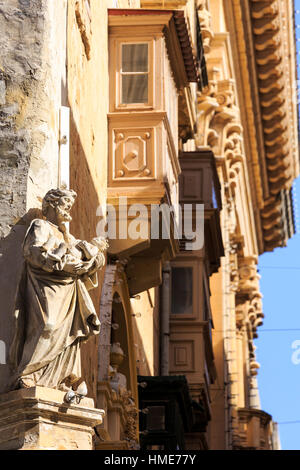 the famous wooden balconies of Valletta old town, Malta with religious statue in the foreground Stock Photo