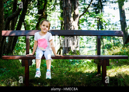 Little Girl is sitting on the bench in the  woods. Active family, parents and children mountaineering in the nature. Stock Photo