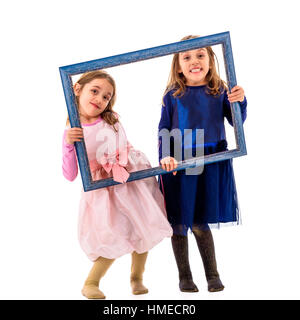 Twin girls are making happy expressions with picture frame. Children posing in studio, fooling around making different facial expressions. Stock Photo