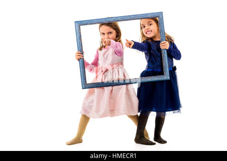 Twin girls are pointing with fingers holding picture frame. Children posing in studio, fooling around making different facial expressions and pointing Stock Photo
