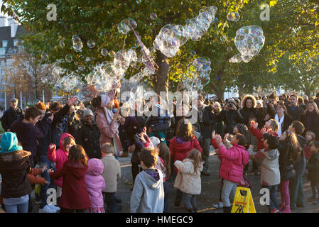 Small children and their parents gather round a street performer leaving a trail of giant bubbles on the South bank in London Stock Photo