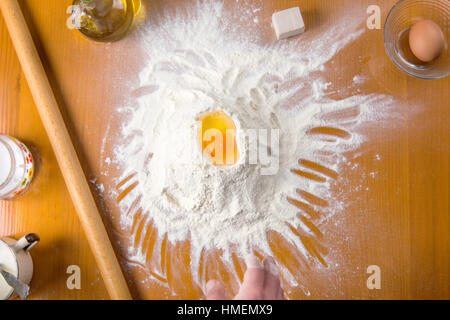 Broken egg on flour pile with baking tools Stock Photo