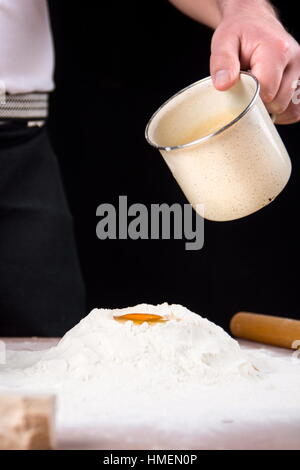 Man pouring milk and yeast on flour. Making pastry Stock Photo
