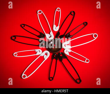 black and white safety pins in circular pattern on red background Stock Photo