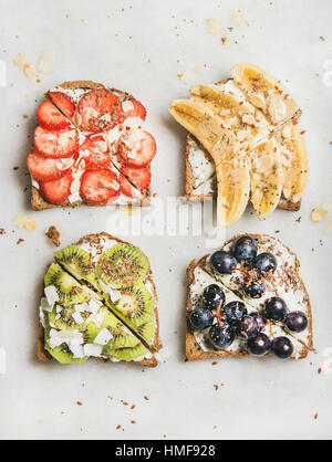 Healthy breakfast toasts. Wholegrain bread slices with cream cheese, various fruit, seeds and nuts. Top view, grey marble background. Clean eating, ve Stock Photo