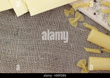 different kinds of pasta and spices on sackcloth and wood Stock Photo