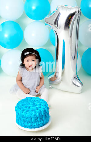 Asian baby girl's first blue birthday cake smashing with balloons decoration. Stock Photo