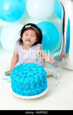 Asian baby girl's first blue birthday cake smashing with balloons decoration. Stock Photo