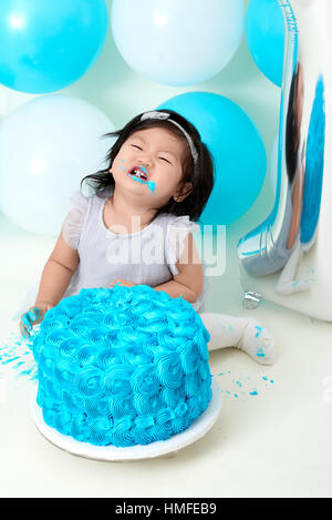 Asian baby girl's first blue birthday cake smashing with balloons decoration. Stock Photo