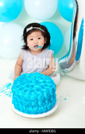 Asian baby girl's first blue birthday cake smashing with balloons decoration. Stock Photo