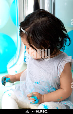 Asian baby girl's first blue birthday cake smashing with balloons decoration. Stock Photo