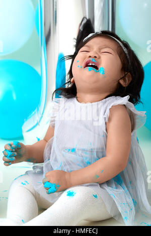 Asian baby girl's first blue birthday cake smashing with balloons decoration. Stock Photo