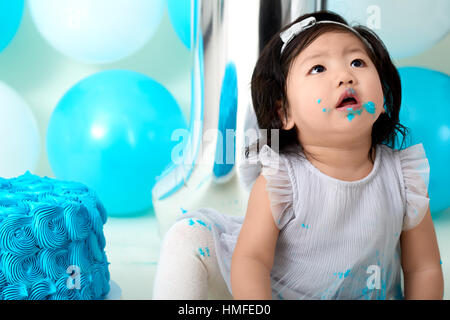 Asian baby girl's first blue birthday cake smashing with balloons decoration. Stock Photo