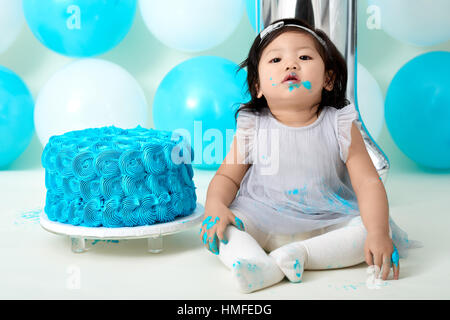 Asian baby girl's first blue birthday cake smashing with balloons decoration. Stock Photo