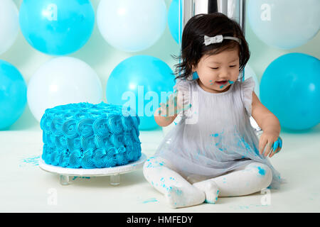 Asian baby girl's first blue birthday cake smashing with balloons decoration. Stock Photo