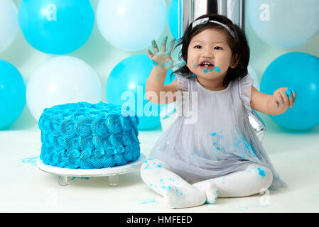 Asian baby girl's first blue birthday cake smashing with balloons decoration. Stock Photo