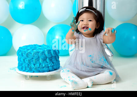 Asian baby girl's first blue birthday cake smashing with balloons decoration. Stock Photo