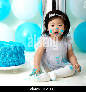 Asian baby girl's first blue birthday cake smashing with balloons decoration. Stock Photo