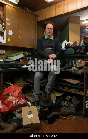 an old fashioned shoe repair / cobbler fixes shoes in his busy shop using traditional techniques and tools Stock Photo