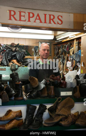 an old fashioned shoe repair / cobbler fixes shoes in his busy shop using traditional techniques and tools Stock Photo
