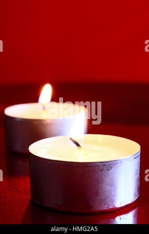 Two burning wax tea candles isolated on a red shiny surface Stock Photo