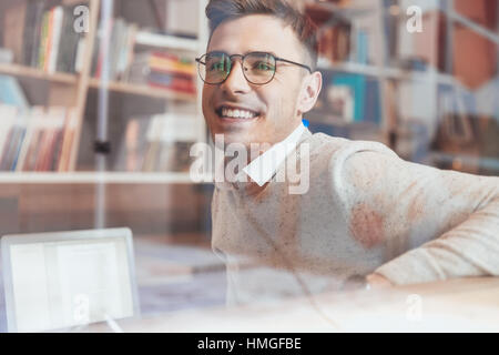 Photo of young cheerful man wearing eyeglasses while sitting in cafe and looking aside. Stock Photo