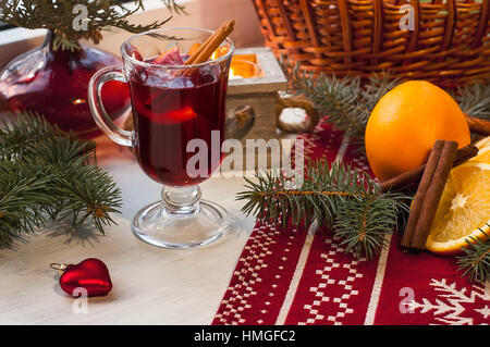 Glass of hot mulled wine on wooden table with candle, orange, cinnamon and christmas tree. Winter holiday, xmas, new year concept Stock Photo