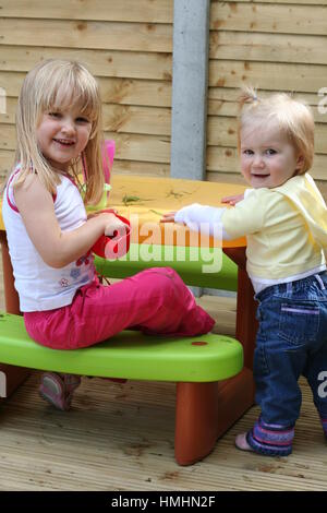 Little blonde girls / children kids playing with sand garden, sitting play table on a bright sunny day sisters playing, family concept  healthy Stock Photo