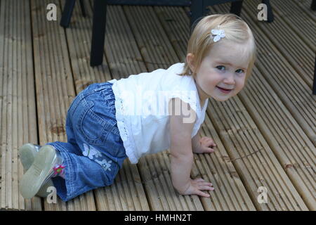 Little girl / Blonde Toddler child kid on all fours crawling on the deck in the garden in the summer time, milestones concept, sweet blonde baby Stock Photo