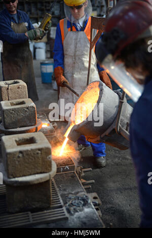 Foundrymen pour molten iron into moulds for making fire grates Stock Photo