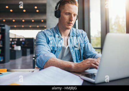 Handsome man studying while sitting at desk with laptop and books. Caucasian male student using laptop for university assignment. Stock Photo