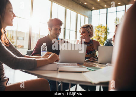 Happy friends using laptop while sitting in class. Group study in university library, doing research on internet. Stock Photo