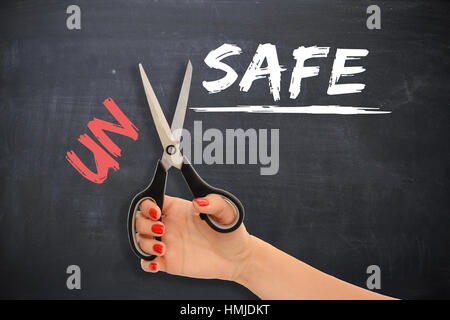 Woman transforming the word “unsafe” into “safe” with scissors Stock Photo