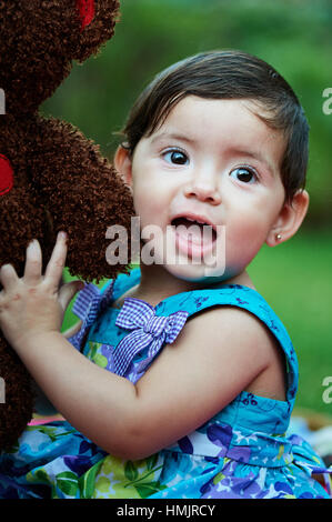 small kid girl hug toy teddy bear in green garden Stock Photo