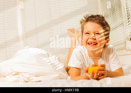 Smiling boy laying in his bed with orange juice Stock Photo