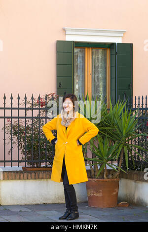 Female tourist posing for a photo in front of house at Burano, Venice, Italy in January