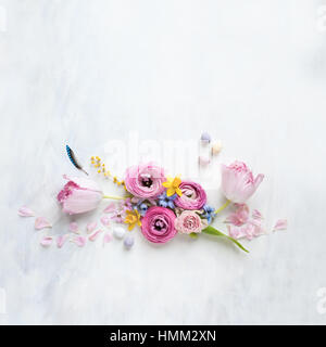 styled still life flat lay with spring flowers, feather and mini eggs arranged in a row on a white and grey textured backdrop Stock Photo