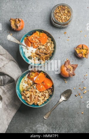 Oatmeal, quinoa granola, yogurt, seeds, honey, persimmon in blue bowls Stock Photo